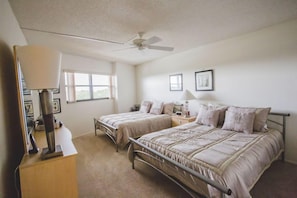 Une chambre avec deux lits simples, un ventilateur de plafond, un bureau avec une lampe et une fenêtre.