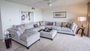A modern living room with a sectional sofa, a glass coffee table, and a ceiling fan. - Gulf and Bay Club- C503 Beautifully updated with great views! (Siesta Key)