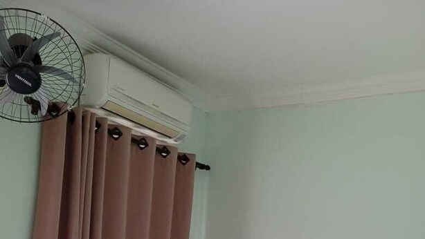 Una habitación pequeña y ordenada con cama, escritorio, refrigerador, ventilador y cortina.