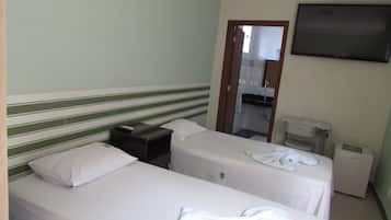 Habitación de hotel con dos camas individuales, una mesita de noche pequeña con un control remoto, un televisor de pantalla plana montado en la pared y un escritorio pequeño con una impresora.