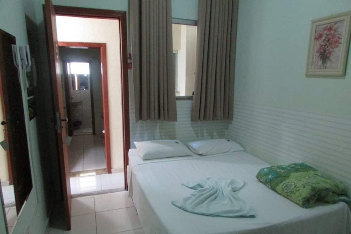 Habitación de hotel con una cama, un cojín verde, una toalla blanca y una puerta que da a otra habitación.