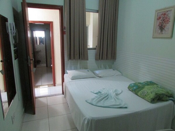 Habitación de hotel con una cama, un cojín verde, una toalla blanca y una puerta que da a otra habitación.