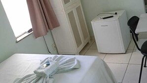 Habitación de hotel con cama, televisión montada en la pared, minibar y ventana con cortinas.