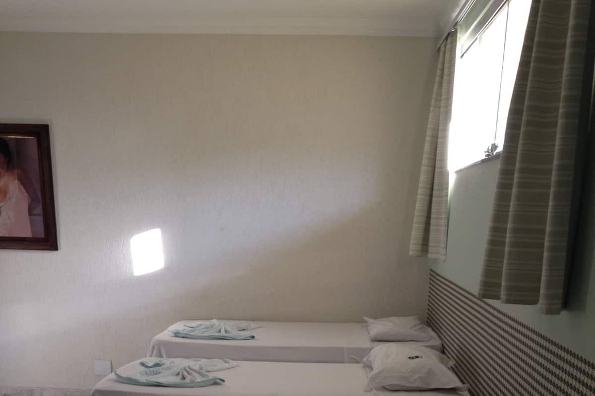Habitación de hotel con cuatro camas individuales, cada una con una almohada y una toalla doblada con pulcritud.