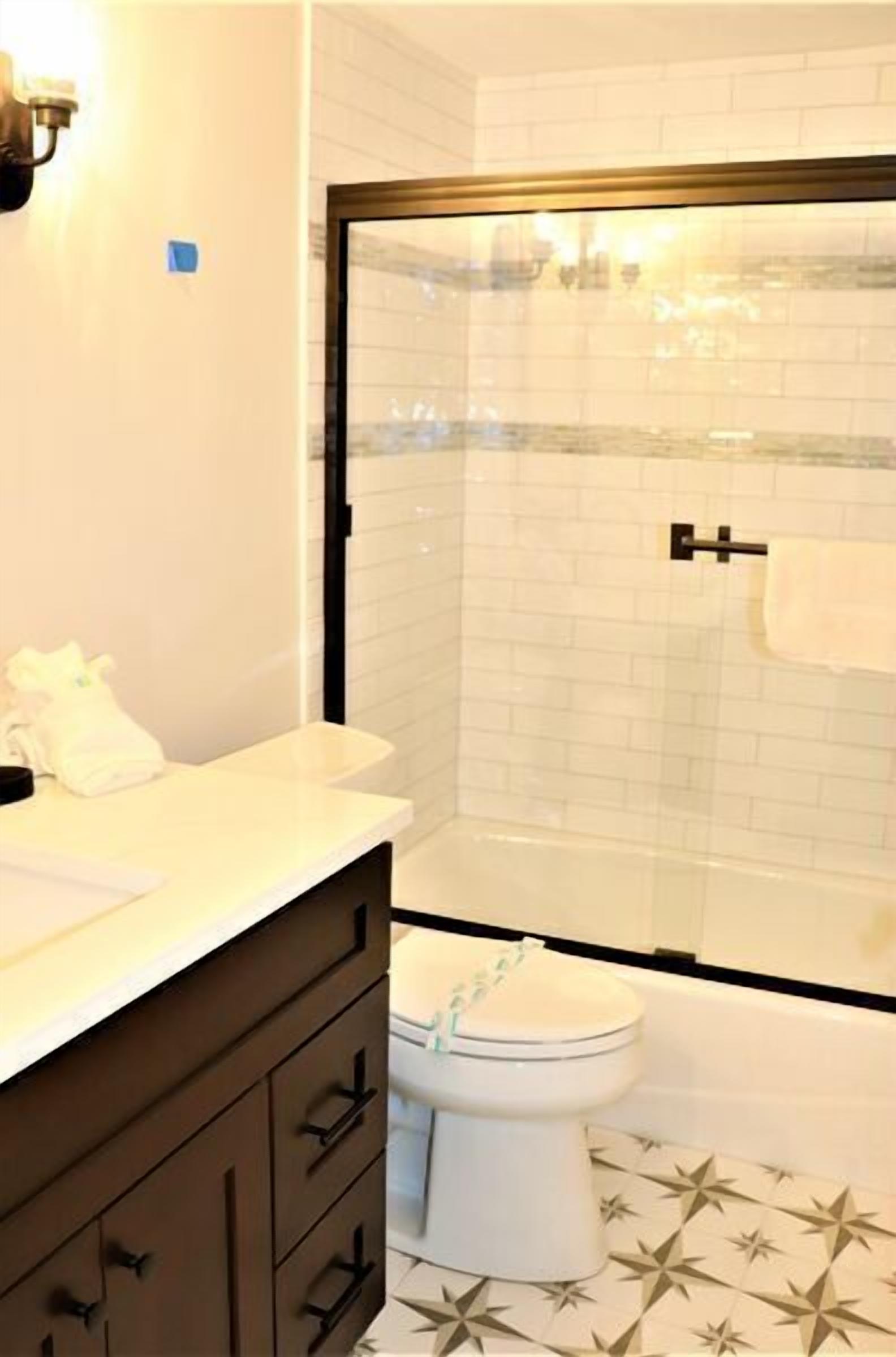 Une salle de bain avec un lavabo blanc, un meuble brun foncé, des toilettes blanches et une cabine de douche en verre.