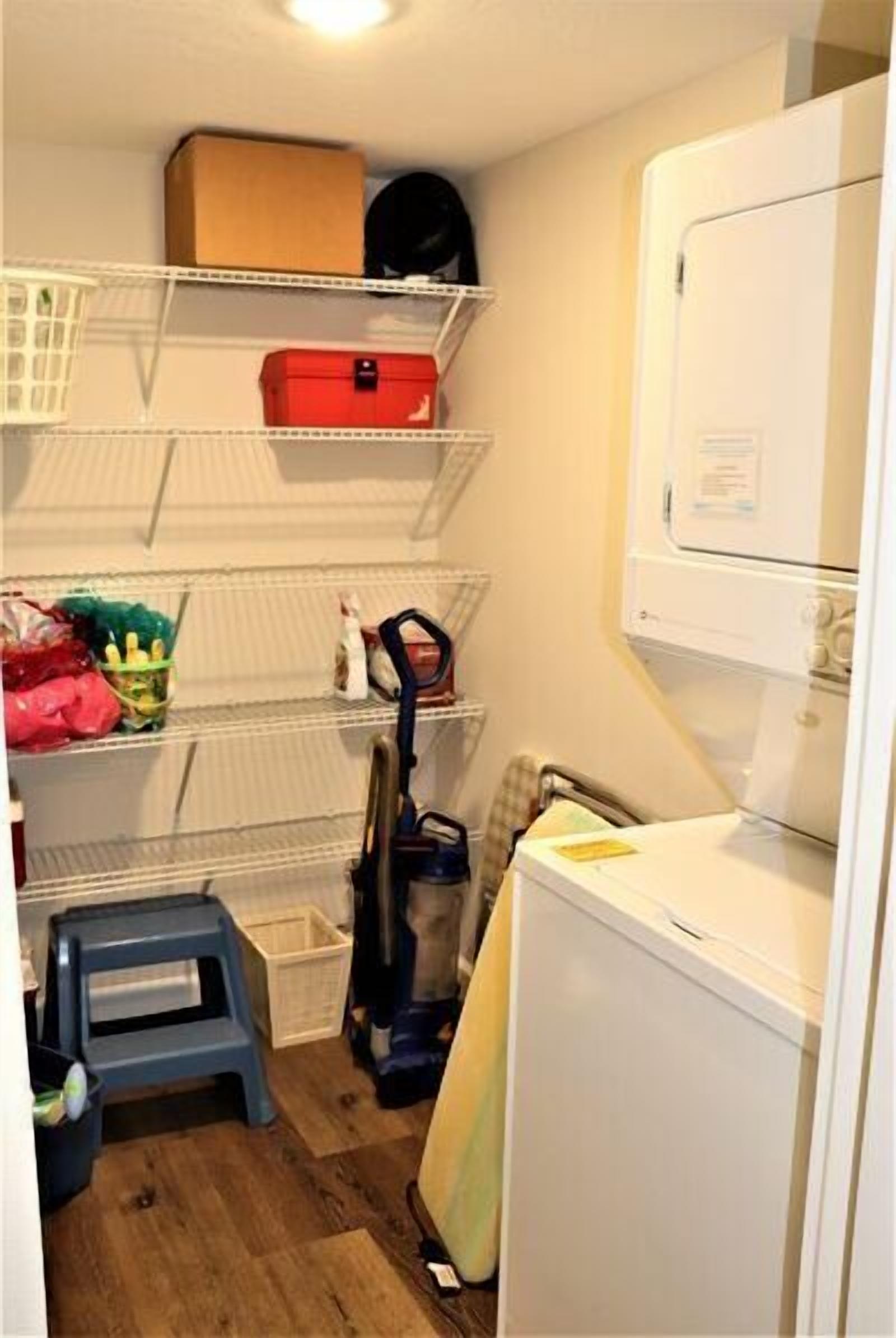 Une buanderie équipée d’étagères, d’un aspirateur, d’une machine à laver et d’un petit tabouret.