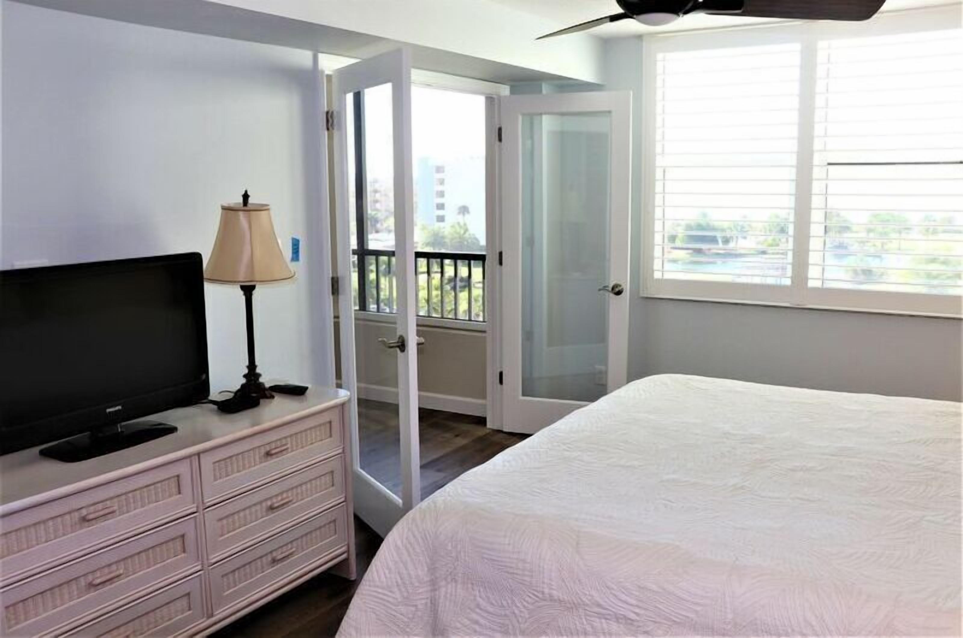 A bedroom with a bed, a dresser, a TV, a lamp, and a balcony door.