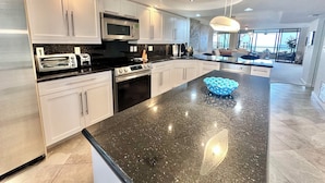A modern kitchen with white cabinets, stainless steel appliances, and a black granite countertop. - Gulf and Bay Club- C702 Beautifully updated! (Siesta Key)