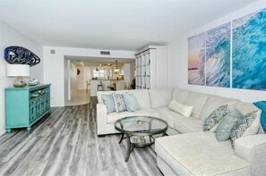 Ein modernes Wohnzimmer mit einer Eckcouch, einem Glastisch und einem türkis-farbenen Schrank.