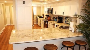 A kitchen with a large island, white cabinets, and a microwave. There are three stools at the island. - Gulf and Bay Club- D209 (Siesta Key)