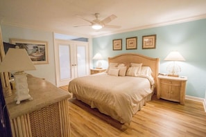 Une chambre à coucher avec un lit, deux tables de chevet, un ventilateur de plafond et une porte.