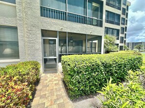 A modern building with a glass entrance, a paved pathway, and well-maintained hedges.