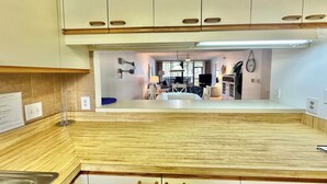 A modern kitchen with wooden cabinets, a central island, and a dining area visible through an open archway. - Lanai and Beach Acess - Gulf and Bay Club E104 (Siesta Key)