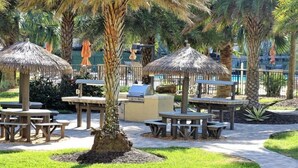 Un espace extérieur aménagé en terrasse, avec des parasols en chaume, des tables en bois et un barbecue.