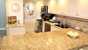 Una cocina con encimeras de granito, armarios blancos, microondas, horno y fregadero.
