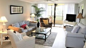 Una sala de estar con sofá, sillones, una mesa de centro, televisión y un balcón con vistas.