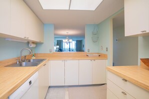 A modern kitchen with a wooden countertop, white cabinets, a built-in dishwasher, and a skylight above the sink.