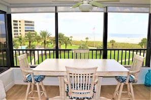 A balcony with a table and chairs, overlooking a beach and a building. - Gulf and Bay Club- E308 Beautiful unit with awesome views! (Siesta Key)