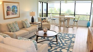 Ein Wohnzimmer mit einer Couch, einem Couchtisch und Sesseln. Es gibt einen Balkon mit Tisch und Stühlen.