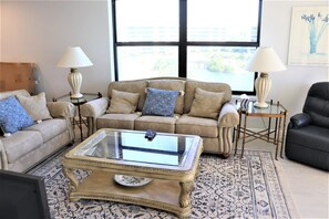 A living room with a beige sofa, a glass-top coffee table, and two lamps.