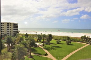 A view of a beach with a hotel in the background, a clear sky, and palm trees. - Gulf and Bay Club- E505 Spectacular views! (Siesta Key)