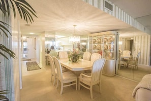 A dining area with a round table and chairs, a glass display case with plates, and a ceiling light. - Gulf and Bay Club- E505 Spectacular views! (Siesta Key)