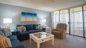 A living room with a blue sofa, a beige armchair, a glass coffee table, and two lamps. - Gulf and Bay Club- E705 Awesome views! (Siesta Key)