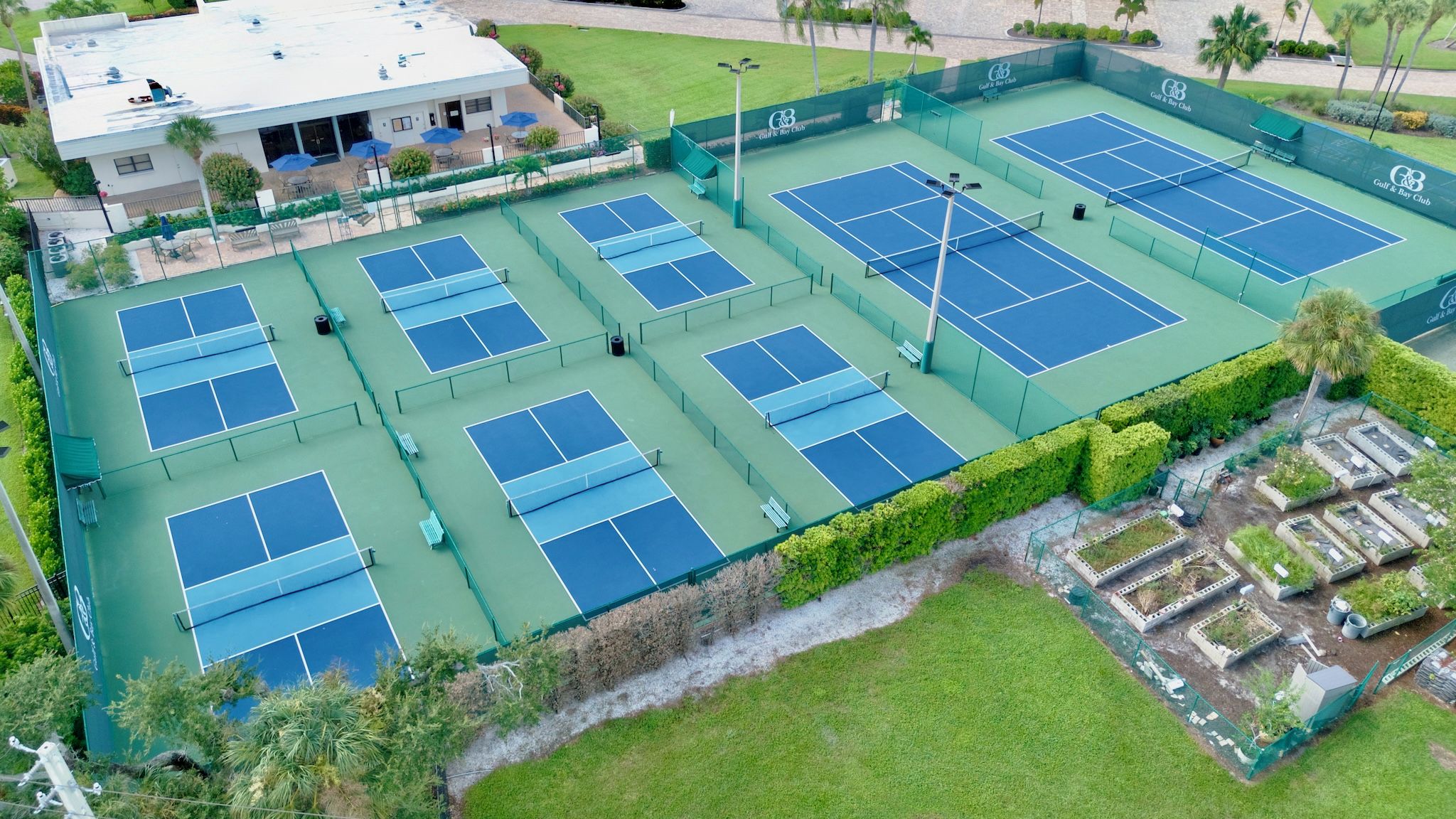 A multi-sport facility with multiple tennis courts, a covered seating area, and a building with a logo.