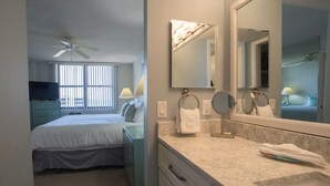 A hotel room with a bed, a bathroom with a sink, mirror, and towel rack. - Gulf and Bay Club- E705 Awesome views! (Siesta Key)