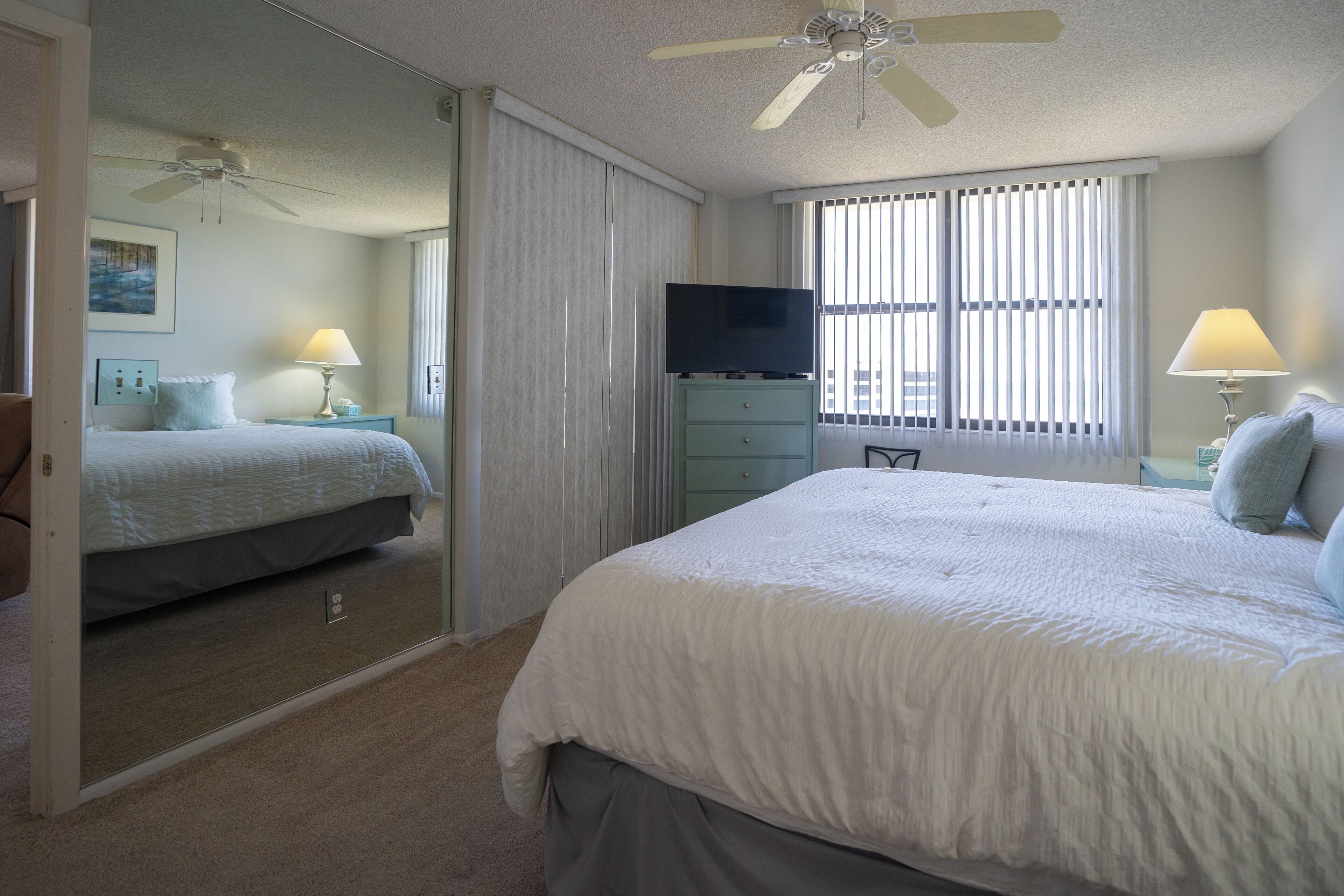 Une chambre à coucher avec un grand lit, un téléviseur posé sur une commode et un ventilateur de plafond.