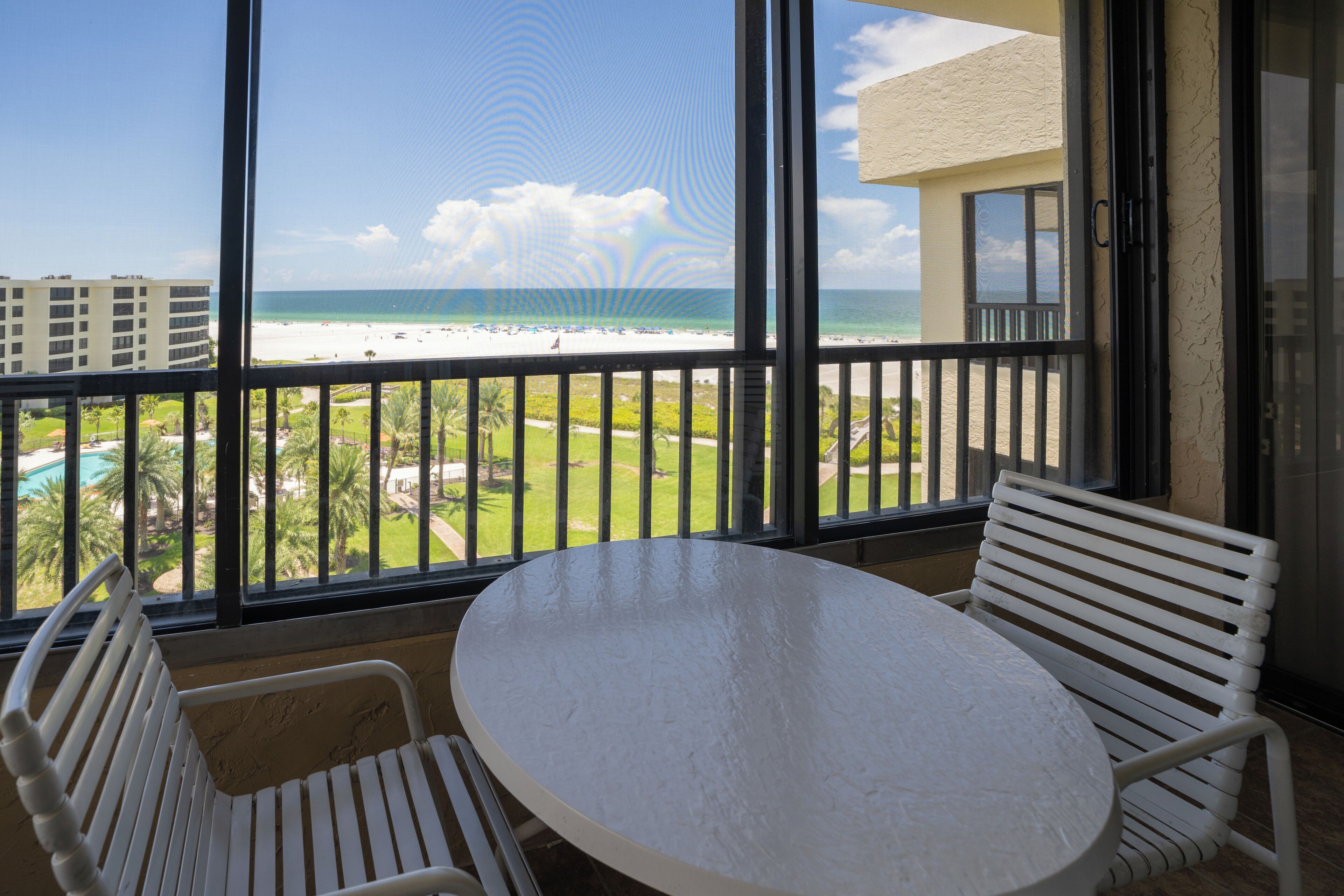 A balcony with a white table and chairs, overlooking a beach and a golf course.