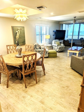 A spacious living area with a wooden dining table, chairs, a sofa, and a TV.