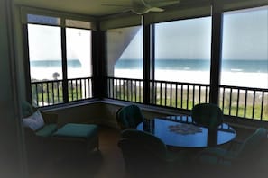 A sunroom with a view of the ocean, a ceiling fan, and a round table with chairs.