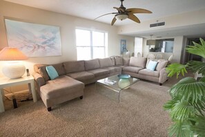 A living room with a sectional sofa, a glass coffee table, a lamp, and a ceiling fan.