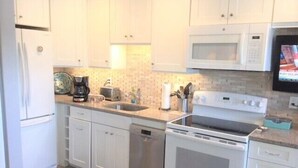 A compact kitchen with white cabinets, a microwave, a stove, and a dishwasher. - Gulf Holiday Unit 12- Close to Beach and Siesta Key Village! (Siesta Key)