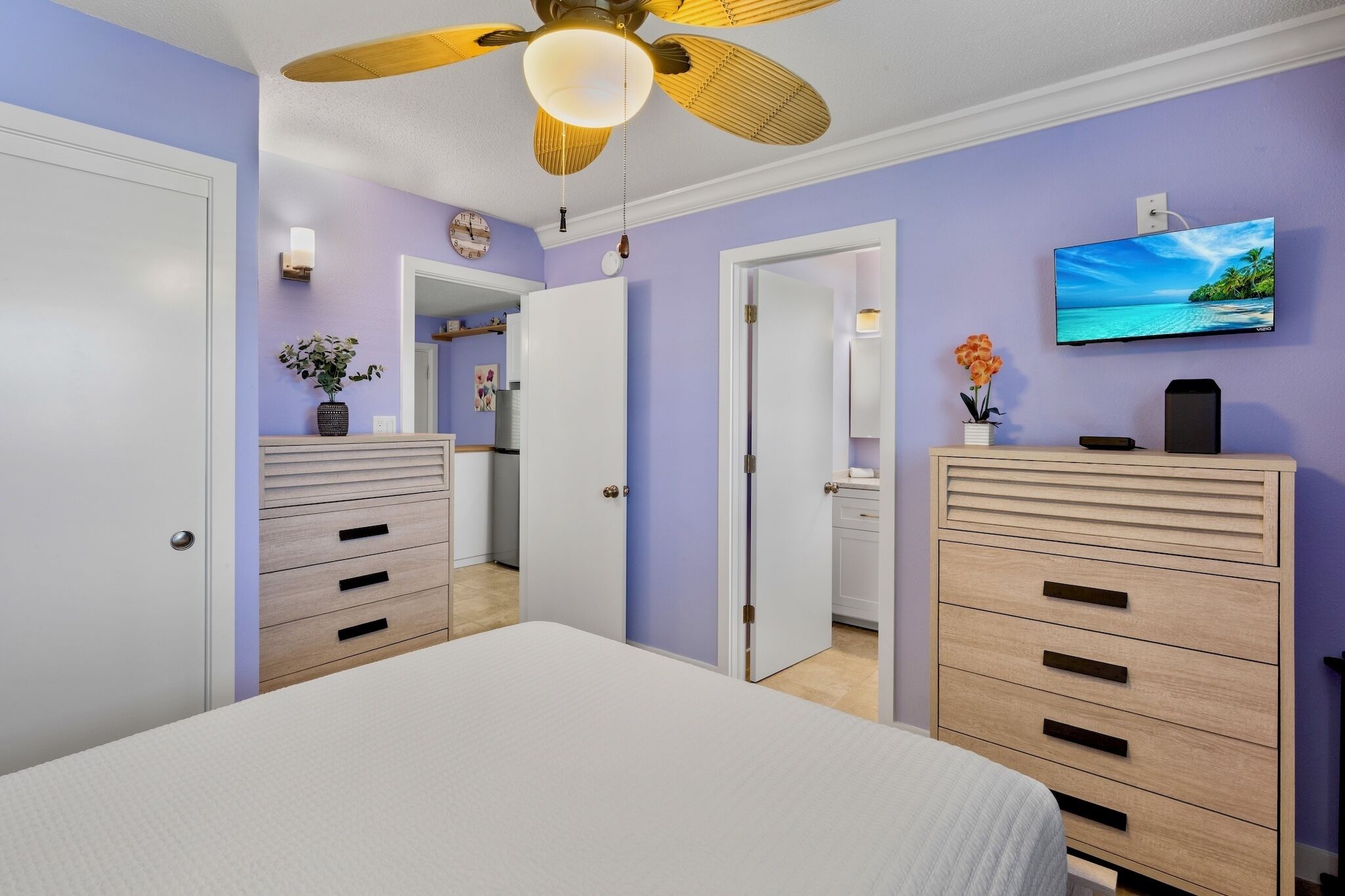 Un dormitorio con cama, ventilador de techo, televisor y cómoda.