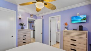 Une chambre à coucher avec un lit, un ventilateur de plafond, une télévision et une commode.