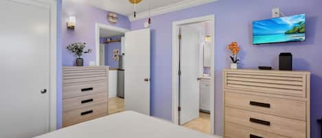 Un dormitorio con cama, ventilador de techo, televisor y cómoda.