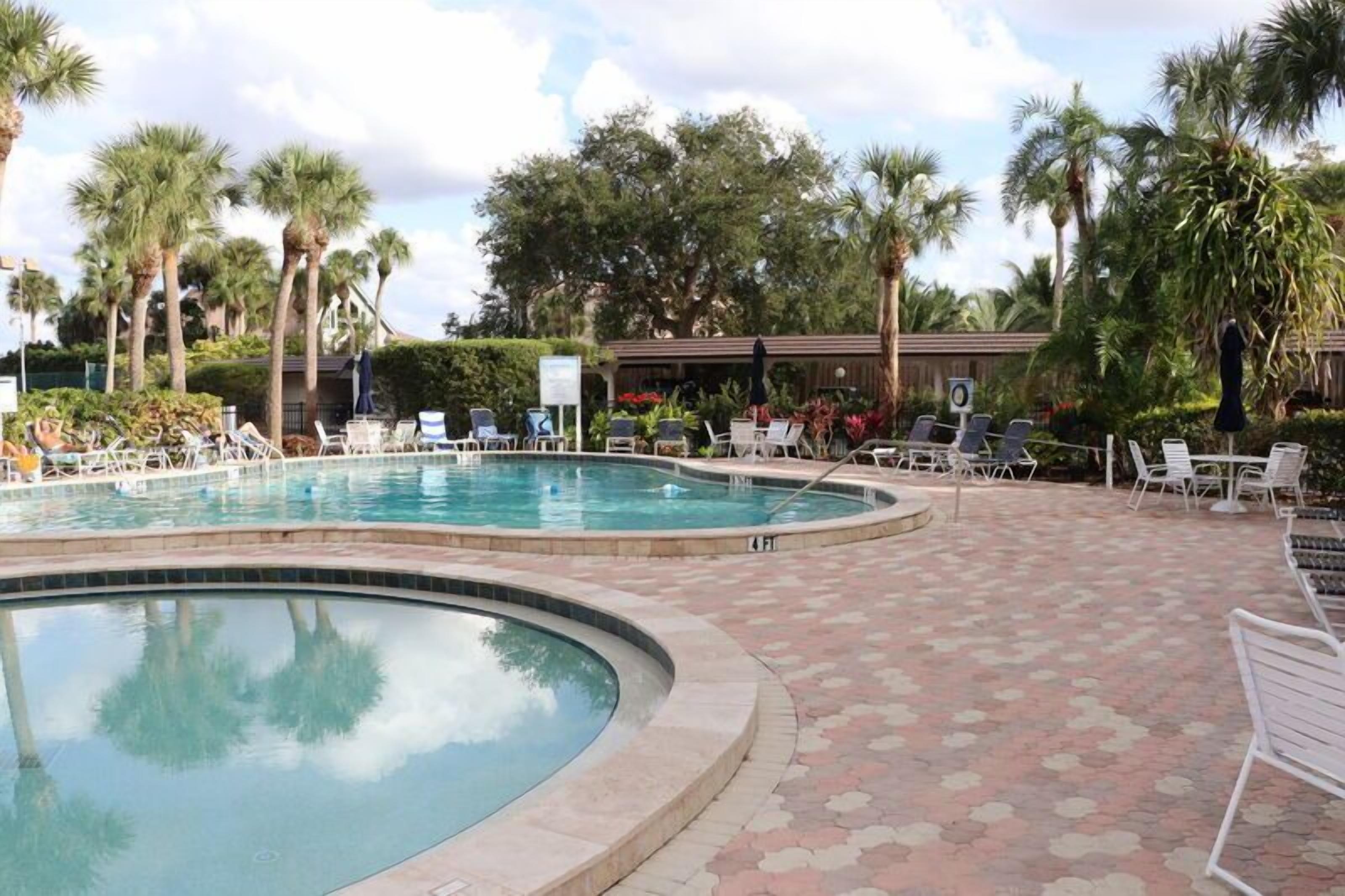 Zona de piscina con sillones de descanso y palmeras.