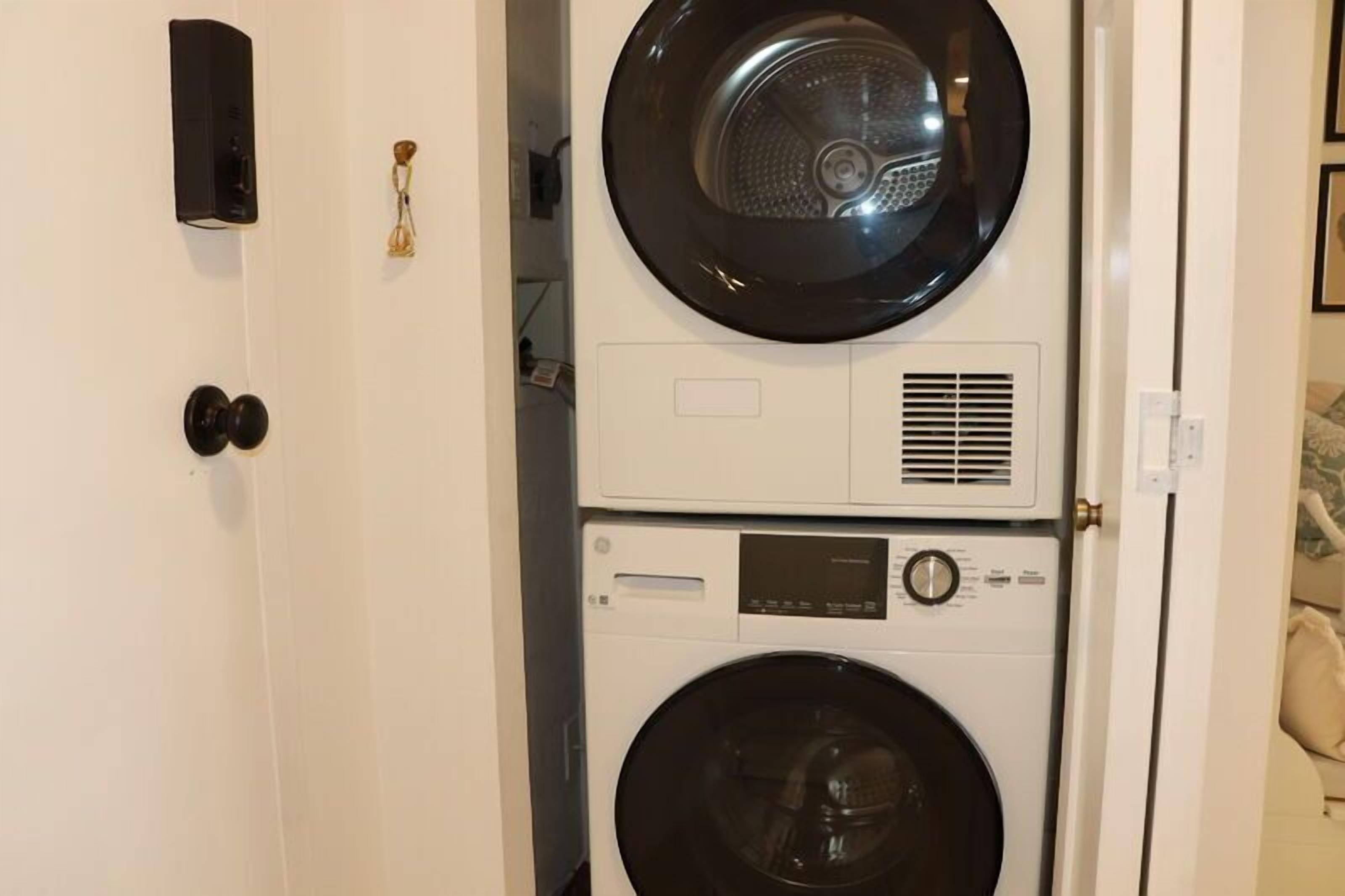 A stacked washer and dryer unit in a room with a white door and a small keychain on the wall.