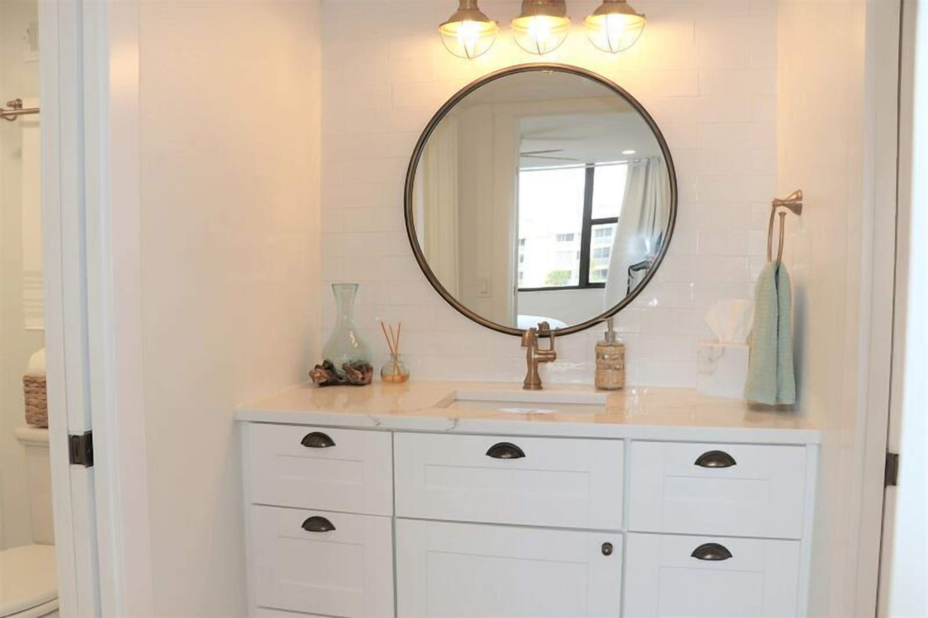 A bathroom with a white vanity, a round mirror, and a light fixture above the mirror.