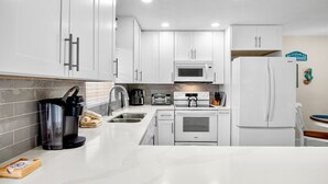 A modern kitchen with white cabinets, a microwave, a refrigerator, and a coffee maker. - Jamaica Royale 1 UPDATED & CLOSEST TO BEACH (Siesta Key)