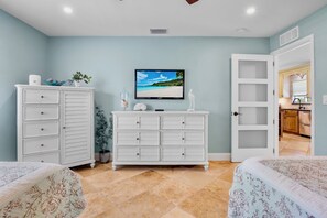 Une chambre à coucher comprenant un lit, une commode, un téléviseur et une porte donnant sur la cuisine.