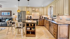 A modern kitchen with wooden cabinets, a central island, and pendant lighting. - Perfect Beachfront Couples Retreat at Jamaica Royale 002 in Siesta Key! (Siesta Key)