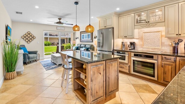 A modern kitchen with a central island, wooden cabinets, stainless steel appliances, pendant lighting, and a view to the outside. - Perfect Beachfront Couples Retreat at Jamaica Royale 002 in Siesta Key! (Siesta Key)