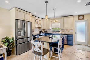 A modern kitchen with a stainless steel refrigerator, double sink, and a central island with bar stools.