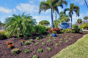 A sign for Jamaica Royale, surrounded by a garden with various plants and palm trees.