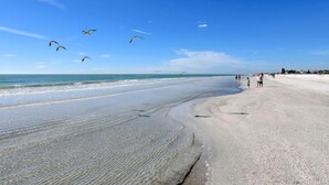 Une plage avec un ciel dégagé, une eau calme et quelques personnes se promenant le long du rivage.