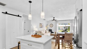 Une cuisine moderne dotée d’un îlot central, de meubles blancs et d’un coin repas avec des chaises en osier.
