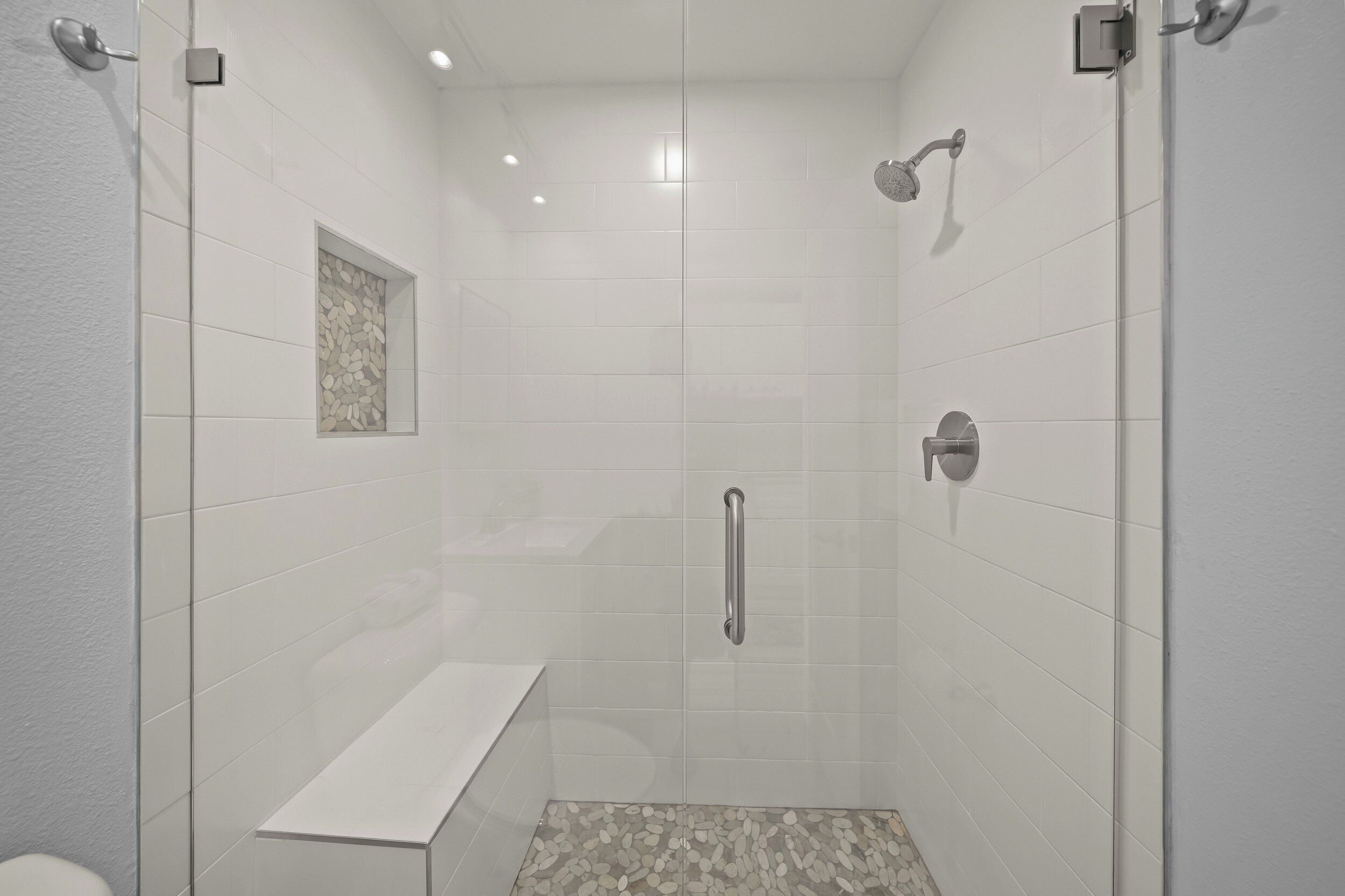 A modern shower area with a glass door, a bench, and a textured floor.